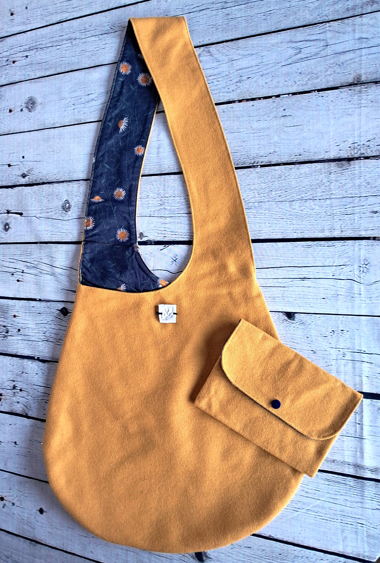 Bolso y estuche handmade wool bag and case set in mustard yellow with navy floral lining, featuring a unique hobo-style design with matching detachable pouch, photographed on weathered blue wooden planks. Sustainable and eco-friendly artisanal accessory crafted from upcycled natural materials.