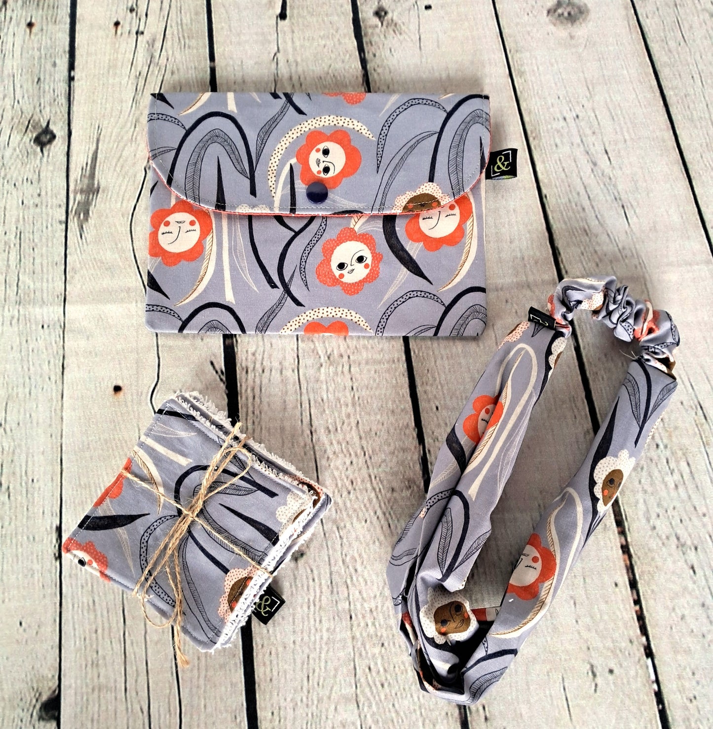 Conjunto higiene set featuring grey and coral pattern with stylized circular designs, including reusable makeup remover pads, matching headband and storage pouch, displayed on whitewashed wooden surface. Handcrafted sustainable beauty accessories made from 100% organic cotton.